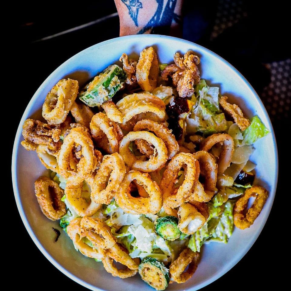 Bowl of crispy fried calamari and vegetables served over a fresh green salad.