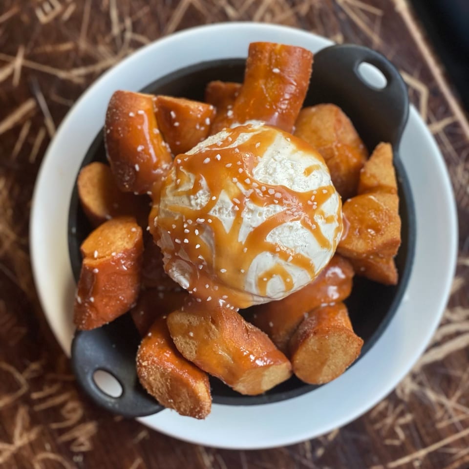 Soft pretzel bites with coarse salt, caramel drizzle, and dipping sauce surrounding a scoop of vanilla ice cream.